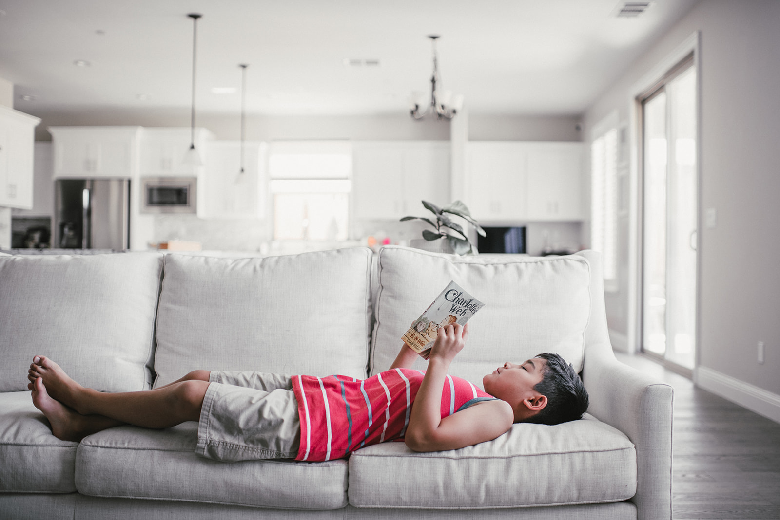 little boy in red laying down and reading on the couch