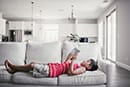 little boy in red laying down and reading on the couch