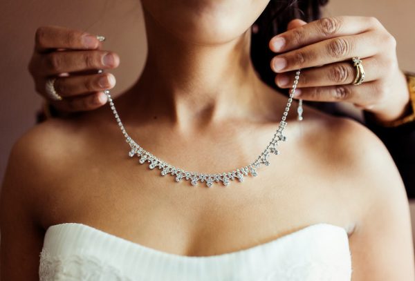 la mariée se fait aider pour mettre son collier