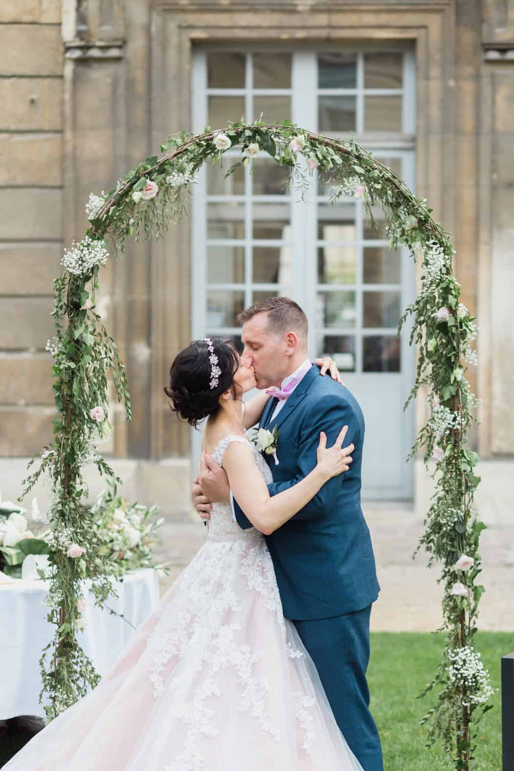 Les mariés s'embrassent sous une arche de fleurs