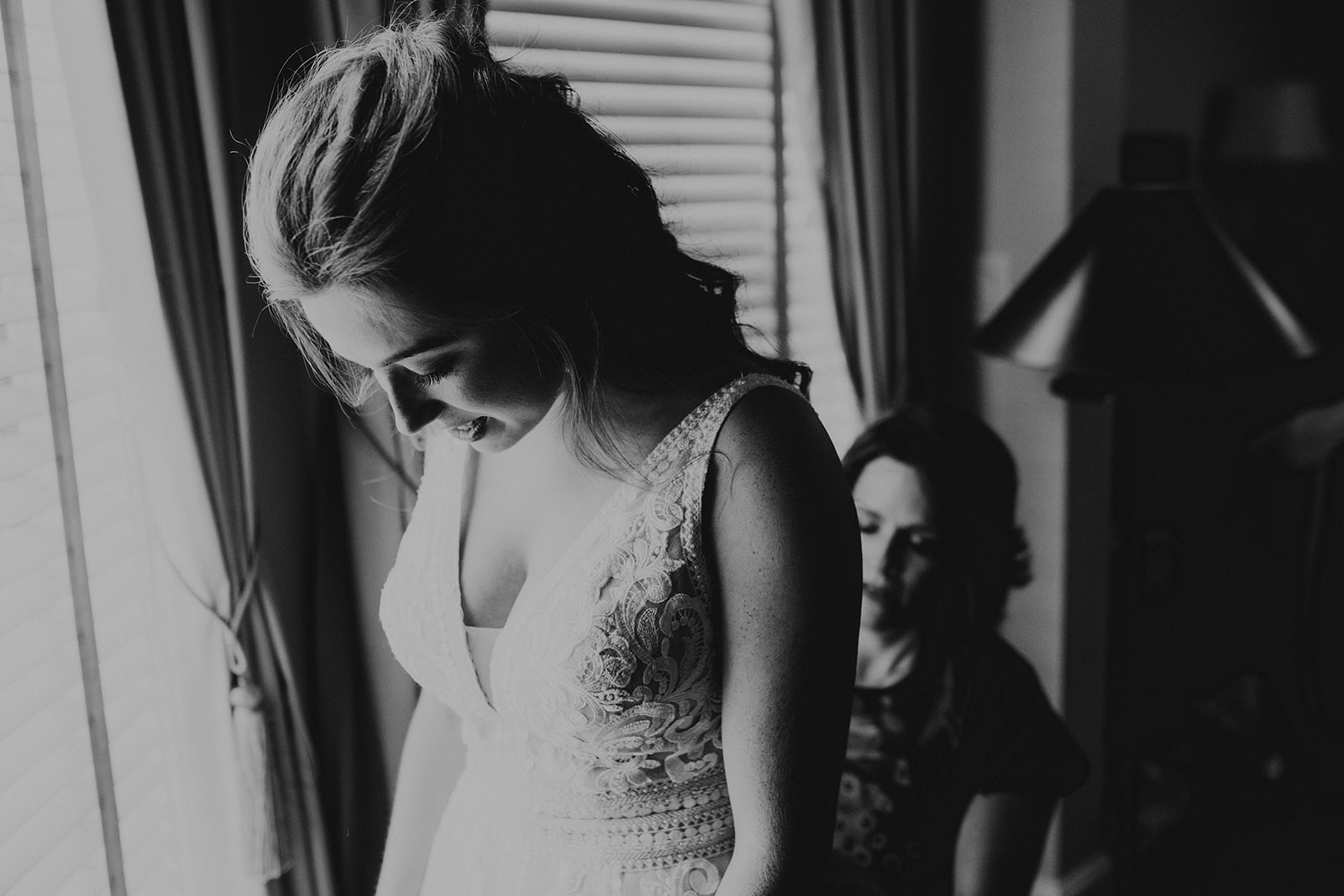 bride looking down while mother buttons her wedding dress