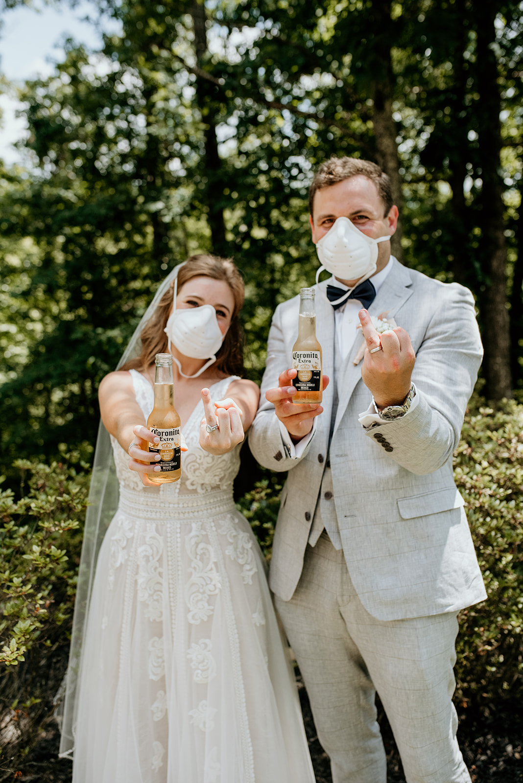 bride and groom with n95 masks on. holding corona beers and holding up ring fingers