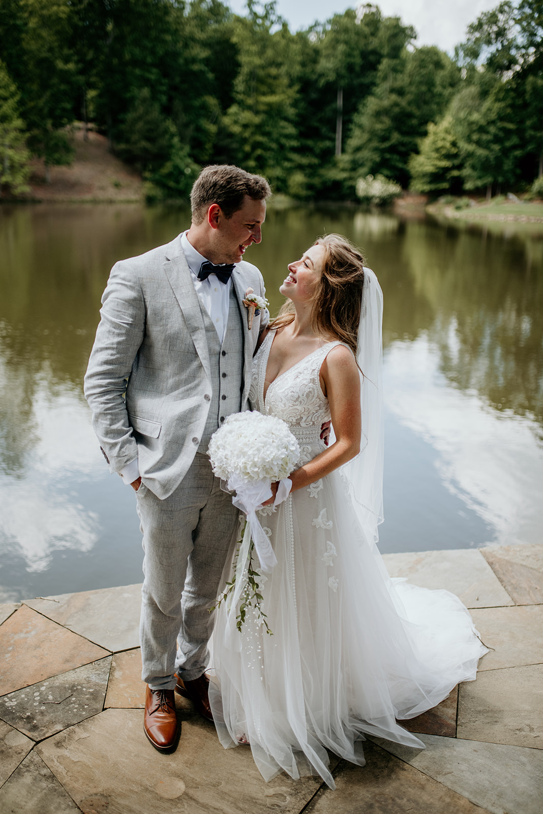 bride and groom on patio above lake, looking at each other smiling