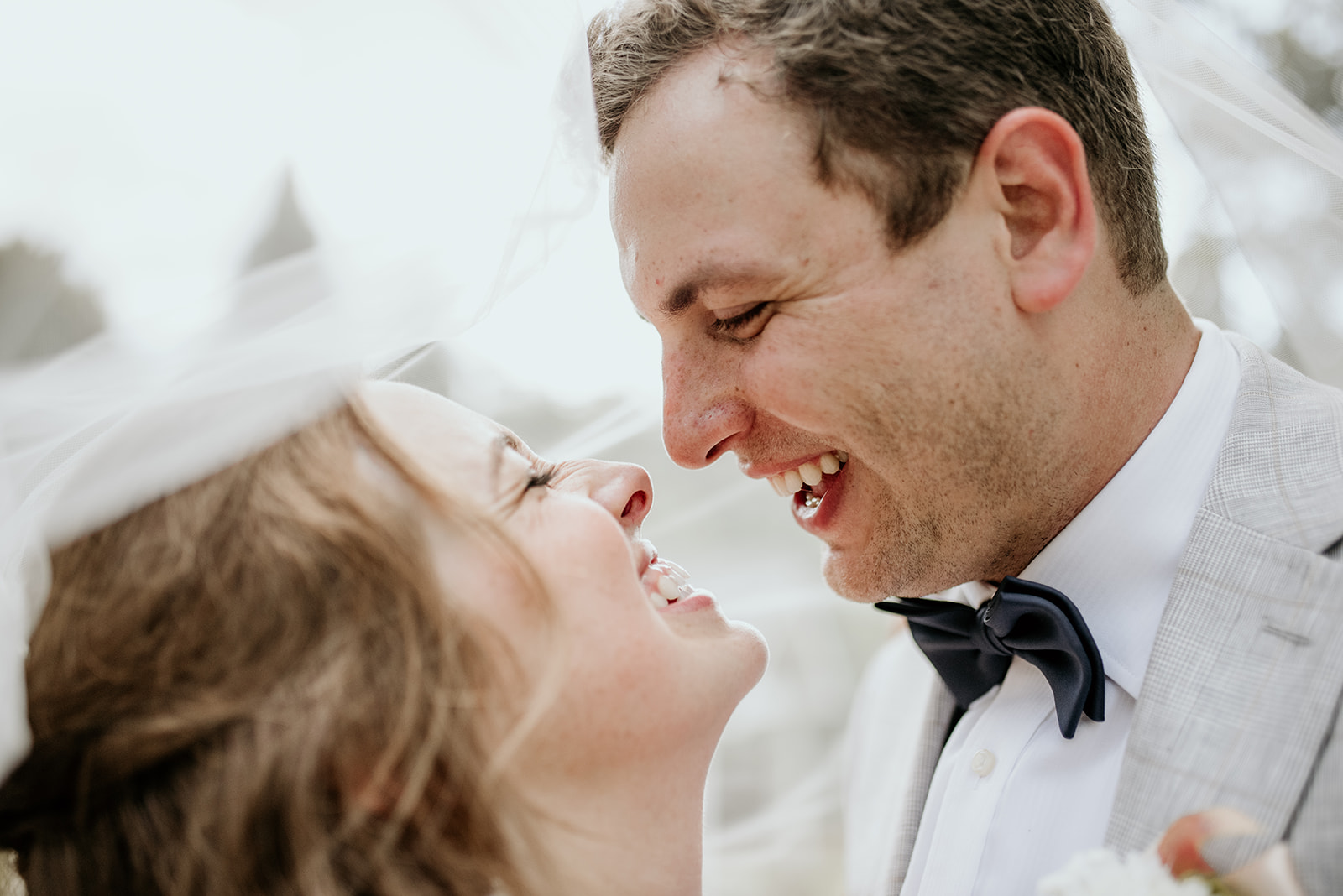 bride and groom under veil looking at each other laughing