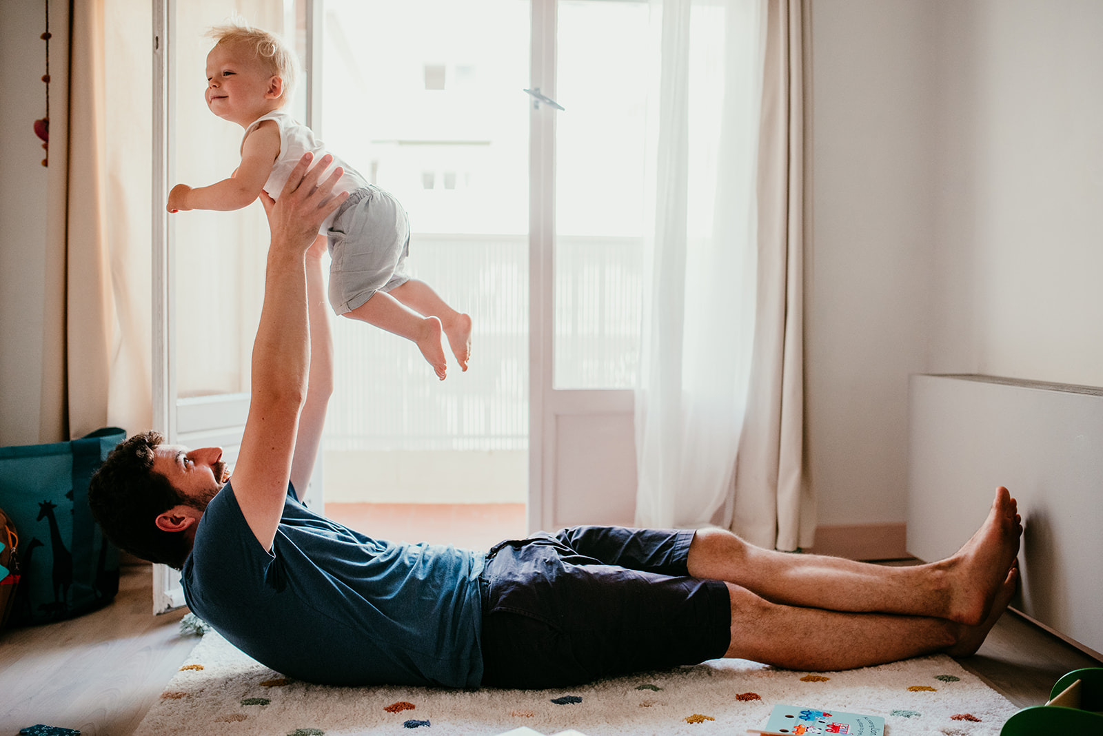 papa est allonge au sol et porte son bebe a bout de bras pour le faire voler