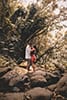 man and woman in floral red dress embracing on rocks on Ka'au Crater Trail engagement session