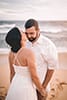 bride kissing husband's cheek holding hands on white sand beach
