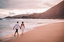 husband and wife holding hands walking along Hawaii shoreline