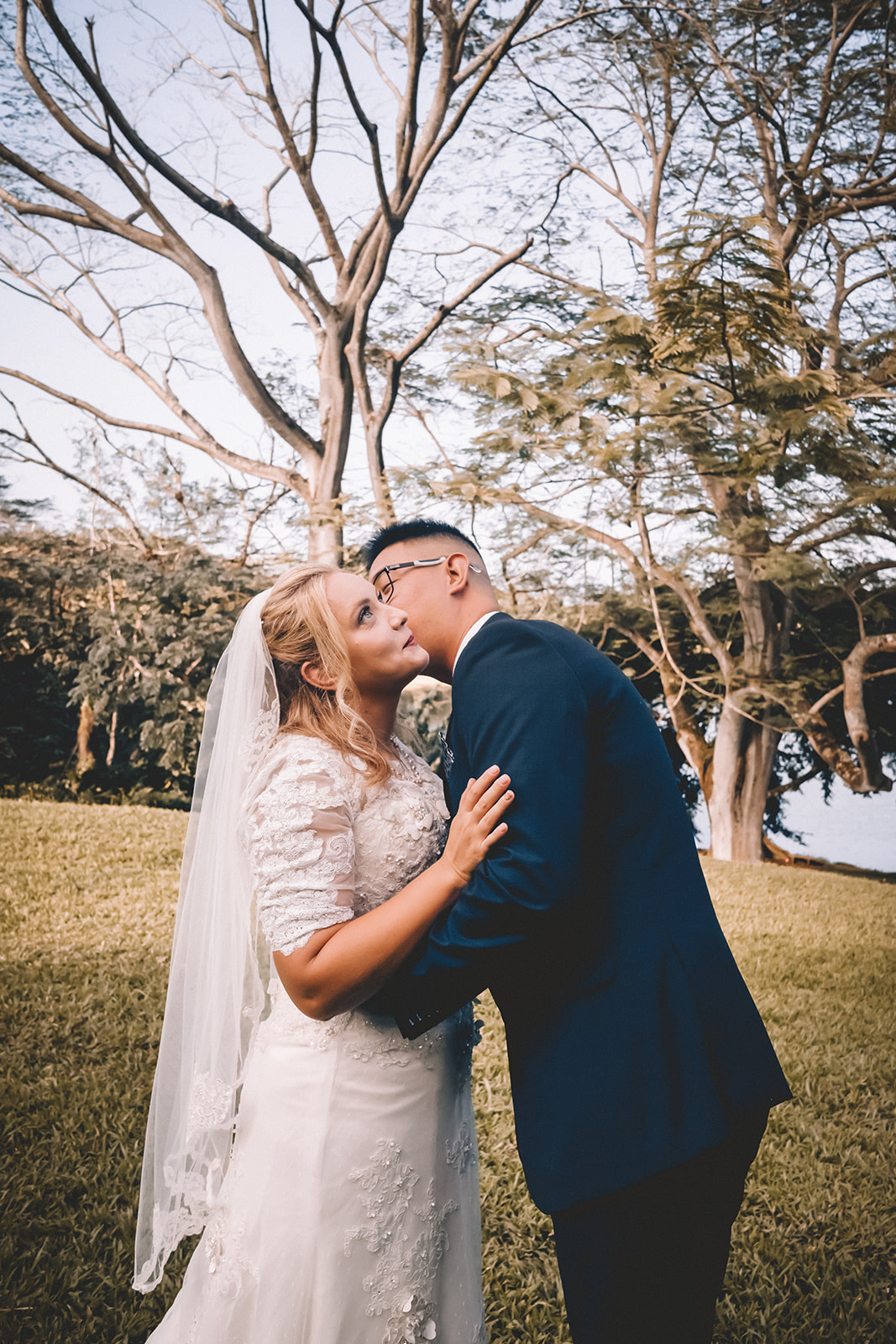 Groom kissing bride to be’s cheek hoomaluhia botanical garden
