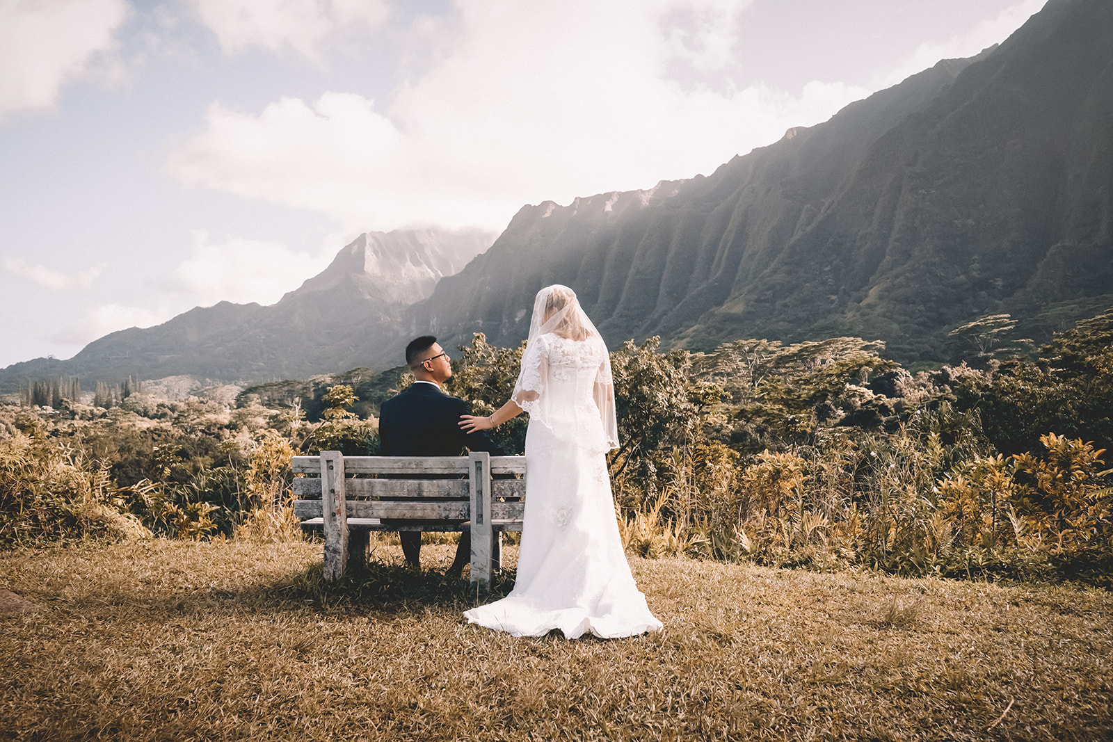 groom sitting on bench bride standing behind groom