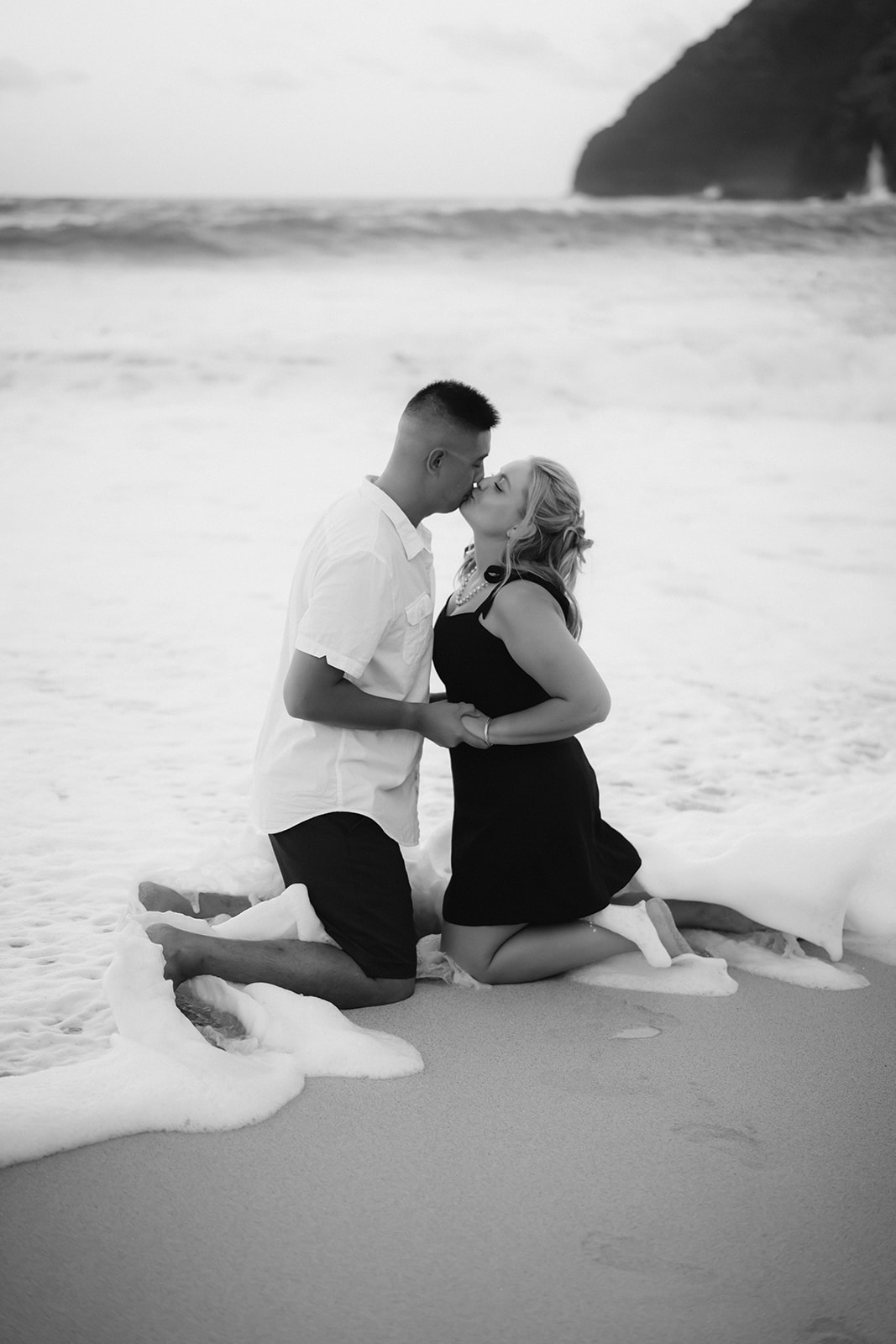 black and white photo couple holding hands kissing at shoreline