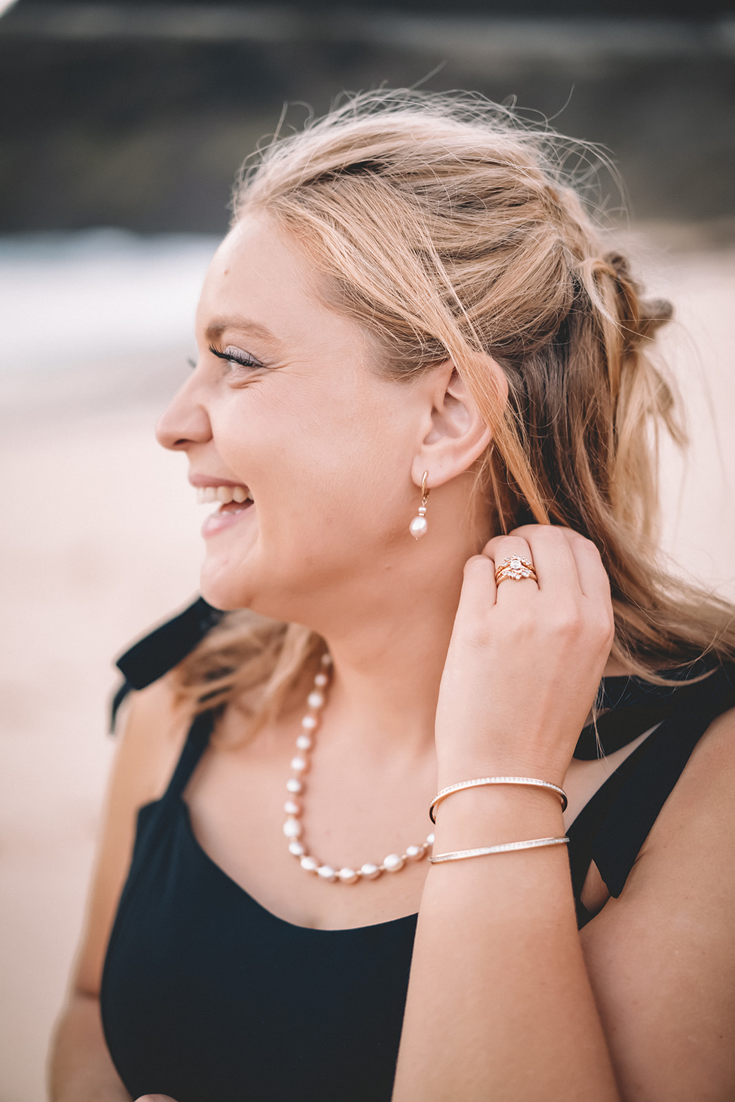 woman pearl earrings necklace smiling looking towards ocean wedding ring